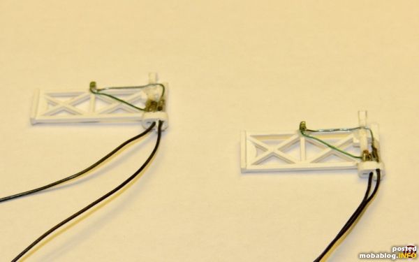 Zur Beleuchtung für den Nachtbetrieb wurden zwei Micro-LEDs vorab mit Anschlüssen versehen und auf die Tore geklebt.
Zur Abdeckung der LEDs wurden winzige Laternengehäuse aus Kupferblech gebogen, lackiert und auf die ...