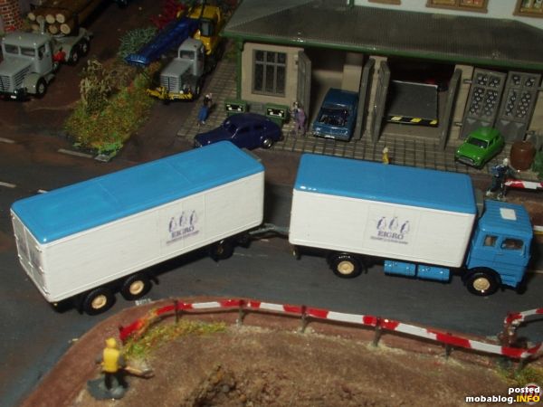 Jetzt ist der Lastzug abfahrbereit, er muß sich eilen, da er den Durchfahrbereich der Gasrohrbaustelle für den Anschlusses des Kühl- und Lagerhauses stark behindert. Rechts im Hintergrund sind ein Speziallangholztransporter ...
