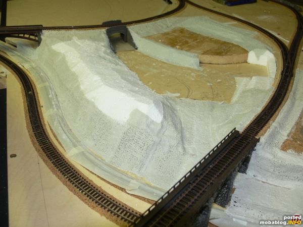 Die Strasse führt vom Tunnel vorbei an dem Plateau, wo später der Kirchhof seinen Platz findet, unter der Brücke hindurch entlang an den Bahngleisen zum Dorf. Rechts vor dem Kirchhof ...