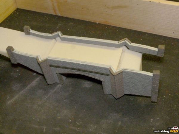 Aus Resten von dunklem Noch-Hartschaum wurden Streifen mit einem Querschnitt von 3x4 mm geschnitten, Mauersteine eingeritzt und stirnseitig in die Aussparungen der Seitenteile eingeklebt. Auf der Straßenebene wurden ebenfalls Mauerstreifen ...