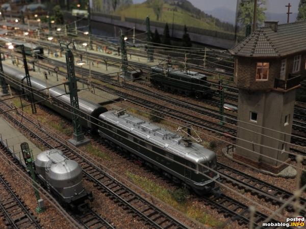 In der Höhe des Stellwerks wartet eine Re 6/6 (Hobbytrain) mit RIC-Wagen (Kato) auf Ausfahrt. Auf dem Abstellgleis im Hintergrund steht eine Ae 4/7 (HAG).