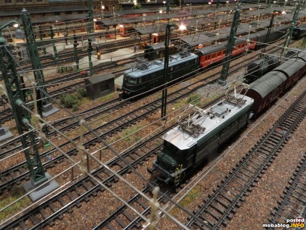 Auf dem Gütergleis durchfährt eine Ae 4/7 mit seitlichen Lüftern (HAG) und Gs-Wagen (Minitrix) den Bahnhof, während die Ae 6/6 mit Chromzierlinien (Fleischmann) und ihrem aus Eurofima- (Arnold) und RIC-Wagen ...
