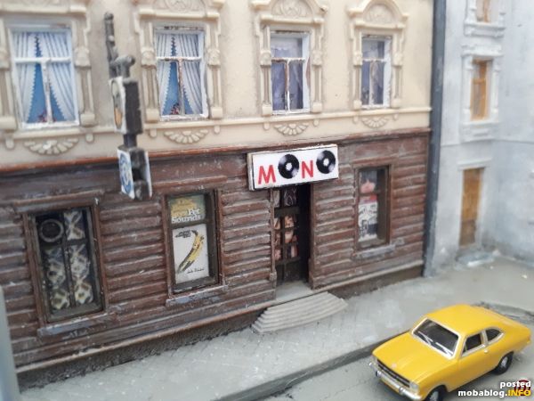 Der Bausatz wurde "manipuliert", so dass eine Türöffnung für einen weiteren Laden entstand. Im Schaufenster: Plakate von zeitgenössischen LPs.