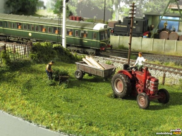 Ein Field Marshall-Traktor mit Hänger (Oxford Diecast) im Einsatz auf der Weide, der Farmer sitzt auf der tuckernden Maschine und gibt dem Helfer seine Anweisungen.