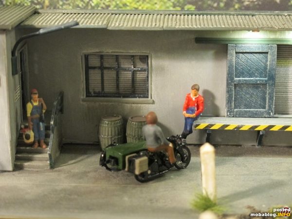 Im Übergangsbereich hin zur angeschlossenen Spedition hockt ein Arbeiter auf der Laderampe und tratscht mit dem British Telekom-Monteur auf seiner Beiwagenmaschine (Oxford Diecast).