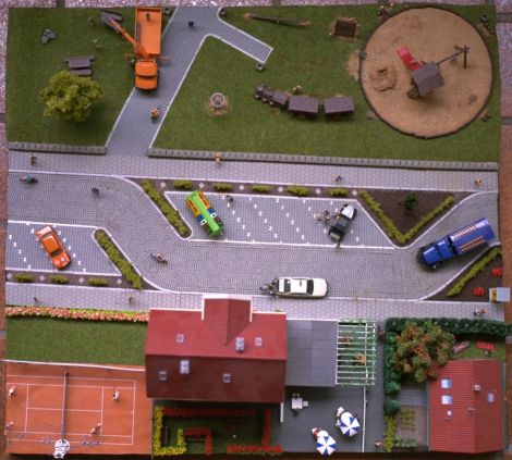 Fangen wir mit einem Überblick über das ganze Diorama an. Neben einem kleinen Einfamilienhaus steht ein Hotel mit Außengastronomie und zugehörigen Tennisplatz. Auf der andere Seite der verkehrsberuhigten Straße befindet ...