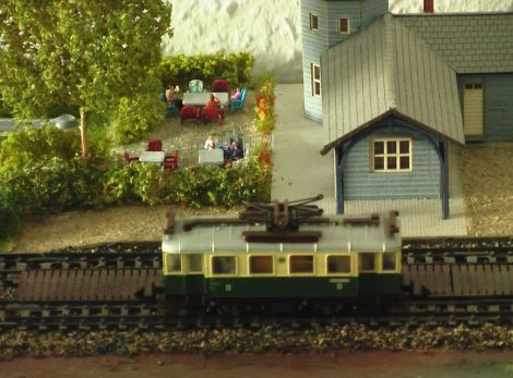 Schläger- und Ball-Ausgabe im Bahnhofsturm. Figuren von Mertens (auf den Bahnen) und Trafofuchs (auf der Gartenterrasse). Im Kinderwagen: "Es ist ein Mädchen!"